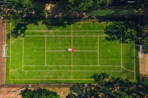Vista aerea di un campo sportivo multifunzione al Trasimeno Glamping Resort in Umbria, Italia, circondato da alberi.