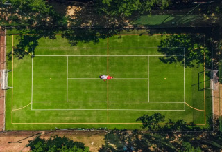 Vista aerea di un campo sportivo multifunzione al Trasimeno Glamping Resort in Umbria, Italia, circondato da alberi.