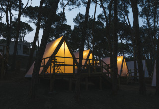 Foto serale di cabine a telaio illuminato tra gli alberi nel parco vacanze Wecamp Cala Montgó in Catalogna, Spagna.