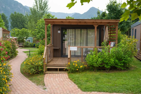 Moderne Cube Suite XL chalet met houten terras, omgeven door bloemen, struiken en bergen op de achtergrond.