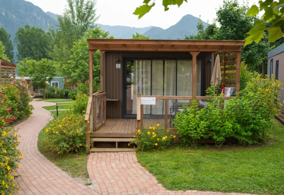 Moderne Cube Suite XL chalet met houten terras, omgeven door bloemen, struiken en bergen op de achtergrond.