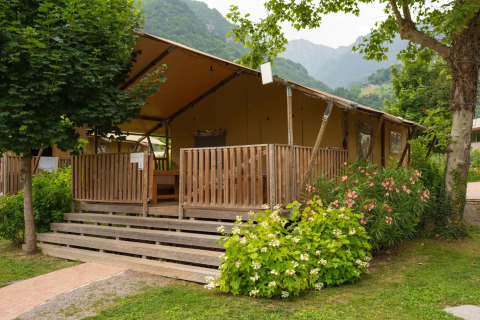 Tienda safari con terraza de madera, rodeada de vegetación, árboles y montañas al fondo.