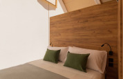 Gemütliches Bett im Safarizelt mit Holzkopfteil, weißen Laken, grünen Kissen und sanftem Licht.