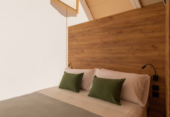 Letto accogliente in tenda safari con testiera in legno, lenzuola bianche e cuscini verdi alla luce naturale.