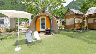 Buitenaanzicht van de Coco Couple pod met parasol, ligstoelen en houten hutten in groene natuur.