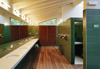 Bagno moderno da glamping con piastrelle verdi, pavimento in legno, lavabi multipli e luce naturale.