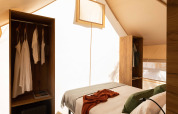 Innenansicht eines Safarizelts mit gemütlichem Bett, offenen Schränken und heller Zeltwand.