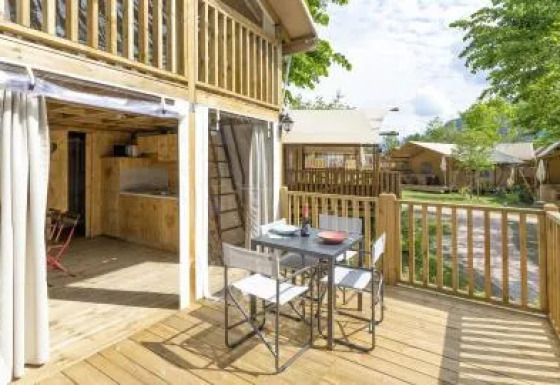 Houten terras met tafel aan Airlodge 2.0, zicht op omliggende lodges en groene omgeving.