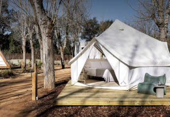 Bell Tent safari tent on a wooden platform among trees, furnished with a bed and cozy outdoor seating area.