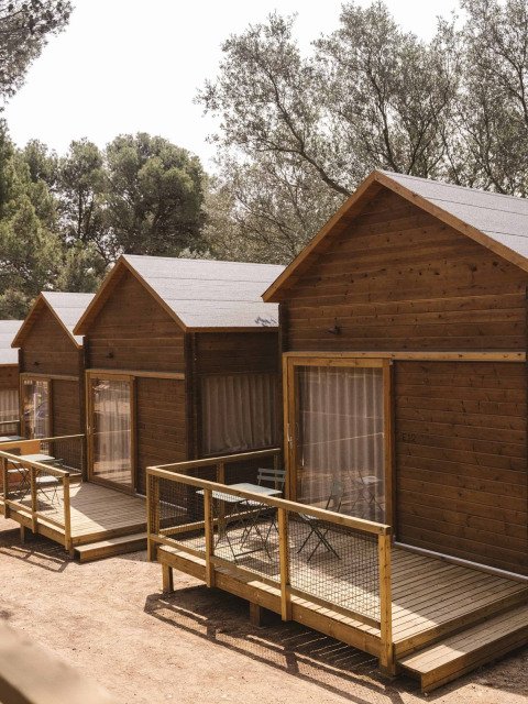 Bungalows de madera alineados con terraza privada y sillas al aire libre, rodeados de vegetación.