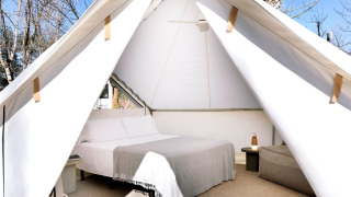 Innenansicht eines Safari-Zeltes mit einem gemütlichen Bett, Nachttisch und Blick auf die Natur.