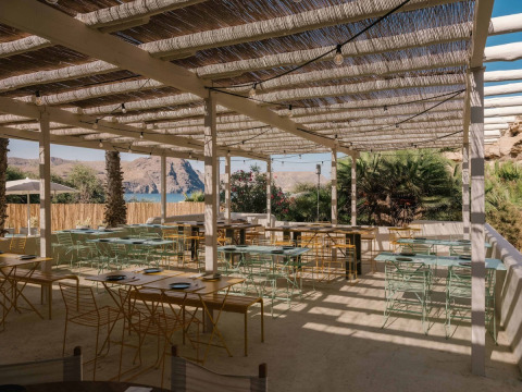 Zona de comedor al aire libre en una tienda safari con muebles modernos y vistas a montañas y lago.