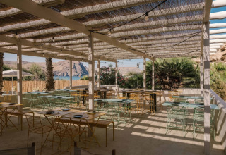Zona de comedor al aire libre en una tienda safari con muebles modernos y vistas a montañas y lago.