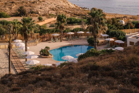Uitzicht op het zwembad van Wecamp Cabo de Gata vakantiepark in Andalusië, Spanje, omringd door palmbomen en zand.