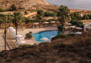 Uitzicht op het zwembad van Wecamp Cabo de Gata vakantiepark in Andalusië, Spanje, omringd door palmbomen en zand.