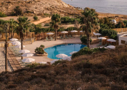 Uitzicht op het zwembad van Wecamp Cabo de Gata vakantiepark in Andalusië, Spanje, omringd door palmbomen en zand.