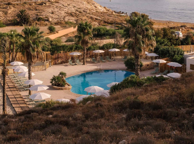 Uitzicht op het zwembad van Wecamp Cabo de Gata vakantiepark in Andalusië, Spanje, omringd door palmbomen en zand.