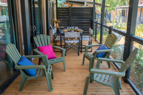 Terraza de madera con sillas verdes y cojines coloridos en Cottage Next XXL Prestige, Trasimeno Glamping Resort, Italia.
