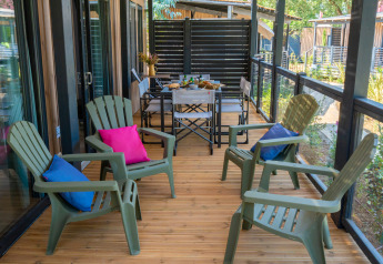 Terraza de madera con sillas verdes y cojines coloridos en Cottage Next XXL Prestige, Trasimeno Glamping Resort, Italia.