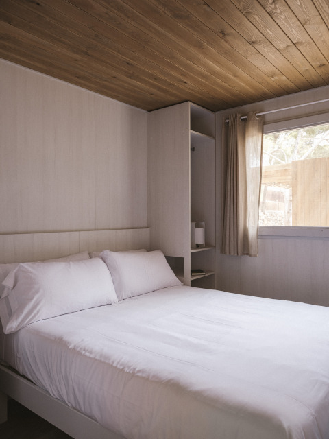 Slaapkamer in de MOBIL HOME FAMILY WOOD bij Wecamp Cala Montgó, Spanje met tweepersoonsbed en houten plafond.