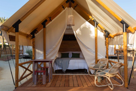 Safari tent Glamping Couple met houten vloer, tweepersoonsbed, buitentafel, stoelen en lamp aan de ingang.
