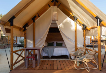 Tenda safari Glamping Couple con pavimento in legno, letto matrimoniale, tavolo, sedie e lampada all'ingresso.
