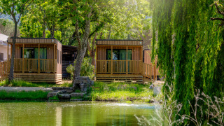 Due cottage in legno sul lago al Cottage Next XL Loggia Laguna, immersi nel verde e nella luce solare.
