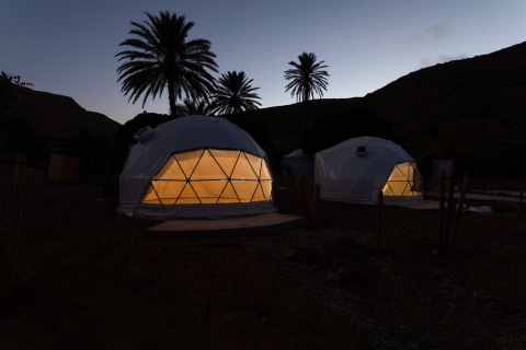 Verlichte geodetische koepeltenten bij schemering in Wecamp Cabo de Gata, Spanje, tussen palmbomen.