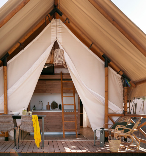 Tienda safari Glamping Comfort con terraza acogedora, mesa de comedor, sillas y cocina interior.