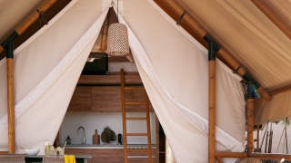 Tente safari Glamping Comfort avec terrasse accueillante, table, chaises et coin cuisine à l’intérieur.