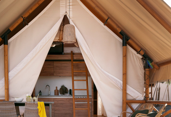 Safari-Zelt Glamping Comfort mit gemütlicher Terrasse, Esstisch, Stühlen und Küchenbereich innen.