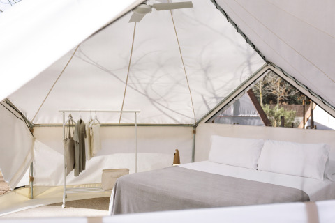 Interior de una tienda glamping moderna con cama doble, perchero, ropa de cama y luz natural suave.