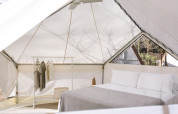 Indersiden af et moderne glamping-telt med dobbelt seng, tøjstativ og naturligt lysindfald.