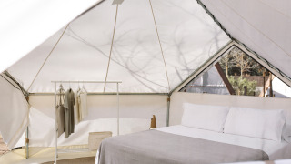 Indersiden af et moderne glamping-telt med dobbelt seng, tøjstativ og naturligt lysindfald.