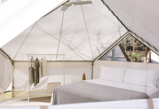 Indersiden af et moderne glamping-telt med dobbelt seng, tøjstativ og naturligt lysindfald.
