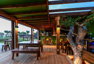 Terrasse en bois à Wecamp Reserva Alecrim en Alentejo, Portugal, avec tables rustiques et arbre naturel à l'intérieur.