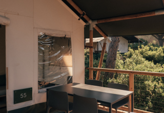 Outdoor dining area on the deck of a safari tent, furnished with modern chairs and nature views.