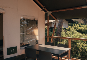 Zona pranzo esterna sulla veranda di una tenda safari, arredata con mobili moderni e vista natura.