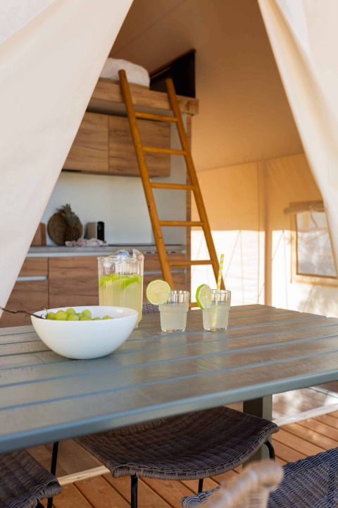 Interieur van een glamping tent bij Wecamp Cádiz, Spanje, met tafel, limonade, druiven, keuken en slaapzolder.