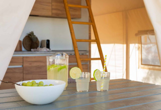 Interieur van een glamping tent bij Wecamp Cádiz, Spanje, met tafel, limonade, druiven, keuken en slaapzolder.