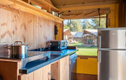 Angolo cottura moderno in una tenda safari con pannelli in legno, frigorifero e vista su altre tende fuori.