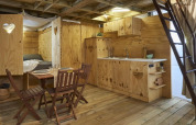 Vista interna di una tenda safari accogliente con arredo in legno, tavolo, cucina e zona notte.