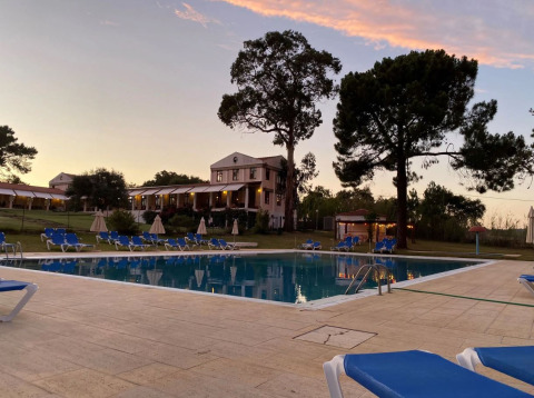 Vista al atardecer de la piscina con tumbonas azules y edificio del hotel al fondo en Wecamp Sao Miguel, Alentejo.