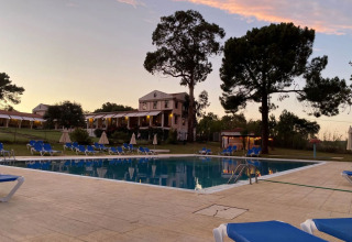 Vista al atardecer de la piscina con tumbonas azules y edificio del hotel al fondo en Wecamp Sao Miguel, Alentejo.
