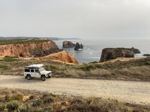Een witte 4x4 rijdt over een grindweg langs ruige kliffen aan de kust nabij Odeceixe, Portugal.