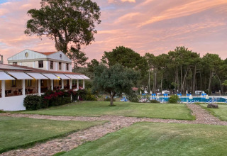 Wecamp Sao Miguel i Alentejo, Portugal: feriepark med grønt græs, træer, pool og charmerende bygning ved solnedgang.