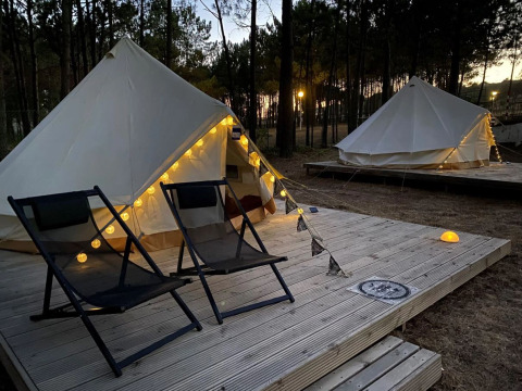 Twee tenten met lichtjes en twee stoelen op houten terras bij zonsondergang in Wecamp Sao Miguel, Alentejo.