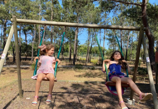 Twee meisjes schommelen samen op een speeltuin tussen de bomen in Wecamp Sao Miguel, Alentejo, Portugal.