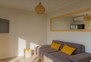 Woonkamer van Bungalow Comfort Family bij Wecamp Reserva Alecrim, Portugal, met zetel en gele kussens.