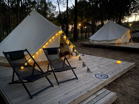 Bell Tent Tipi-Zelte mit Lichterketten und Stühlen auf Holzplattform, idyllisch im Wald bei Dämmerung.